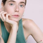 Detox Diet - Woman in Green Tank Top Sitting Beside Table With Drinking Glass and Fresh Vegetables