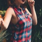 Vegan Makeup - Side view of young eccentric female with ginger hair and dark makeup in checkered dress standing in garden near boxes with assorted fresh vegetables and fruits