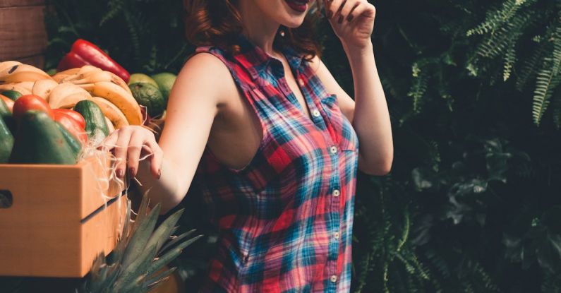 Vegan Makeup - Side view of young eccentric female with ginger hair and dark makeup in checkered dress standing in garden near boxes with assorted fresh vegetables and fruits