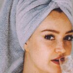 Healthy Hair Ends - Young woman with hair wrapped with towel and bared shoulders drinking water and looking at camera