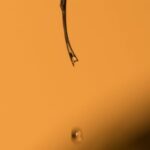 Essential Oils Hair - Closeup of dark hair with liquid falling on yellow background with blurred shadow