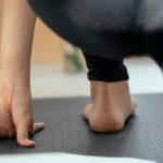 Holistic Wellness - Back view of crop unrecognizable flexible female stretching legs and practicing yoga in Crescent Lunge on the Knee pose at home