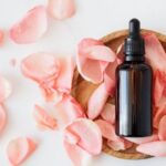 Natural Perfumes - Top view of empty brown bottle for skin care product placed on wooden plate with fresh pink rose petals on white background isolated