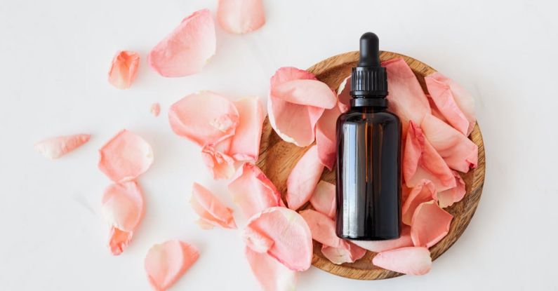 Natural Perfumes - Top view of empty brown bottle for skin care product placed on wooden plate with fresh pink rose petals on white background isolated