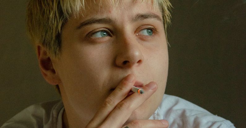 Microneedling Face - A young man with blonde hair smoking a cigarette