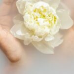 LED Therapy - Unrecognizable female with soft manicured hands holding white flower with delicate petals in hands during spa procedures
