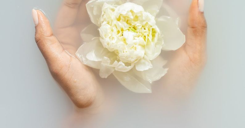 LED Therapy - Unrecognizable female with soft manicured hands holding white flower with delicate petals in hands during spa procedures