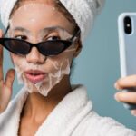 Skincare Devices - Confident black female with sheet mask taking selfie on smartphone