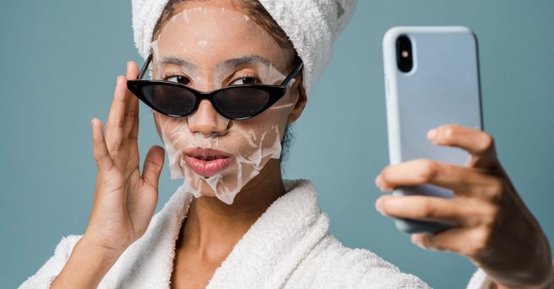Skincare Devices - Confident black female with sheet mask taking selfie on smartphone